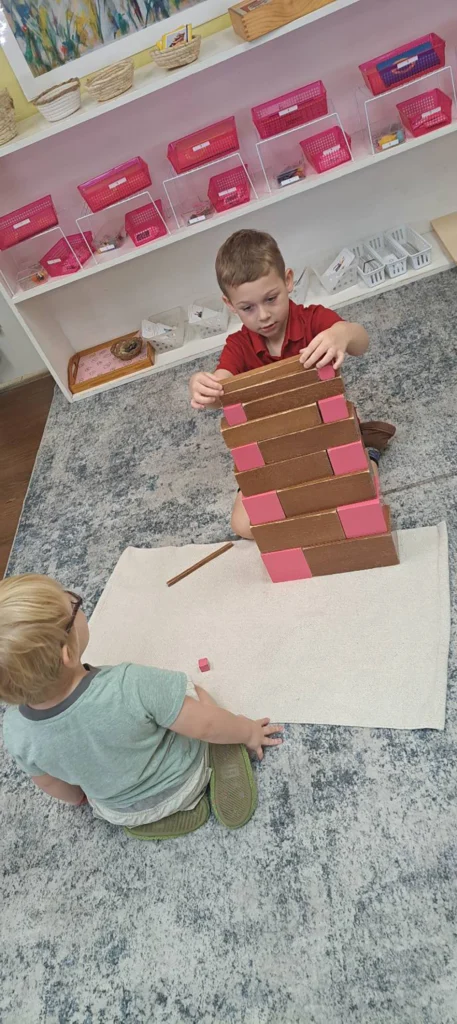 Child stacking Montessori brown stair materials on a classroom rug