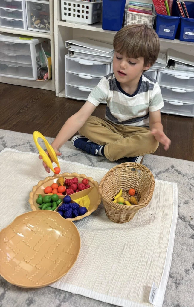 Child using tongs to sort colorful objects into a basket