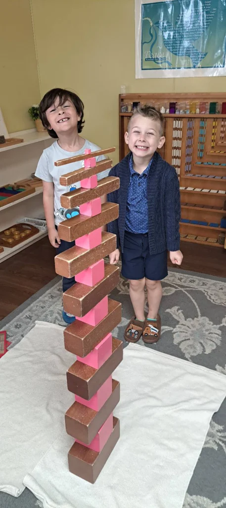 Two students standing beside a tall tower built with Montessori materials