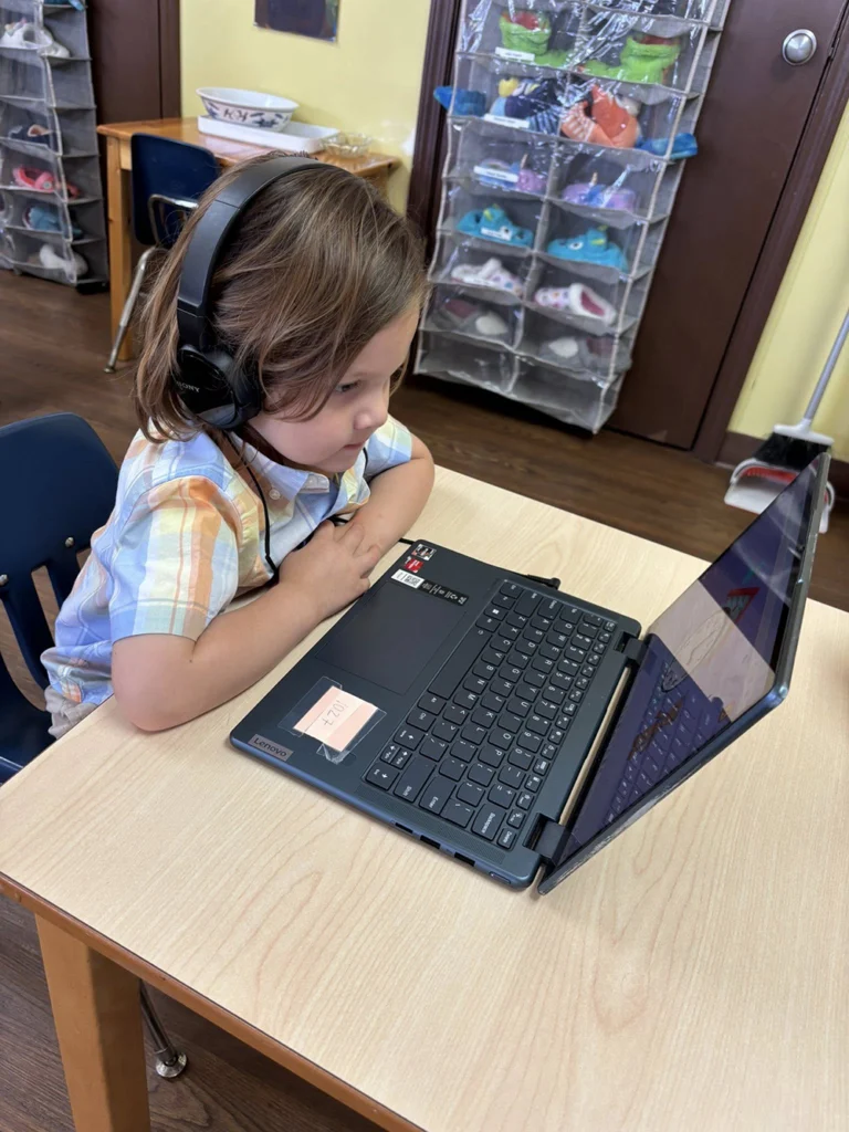 Child wearing headphones while using a laptop at a classroom table