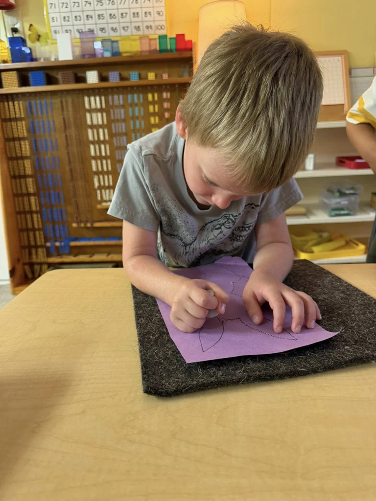 Child tracing shapes on paper during a Montessori classroom activity