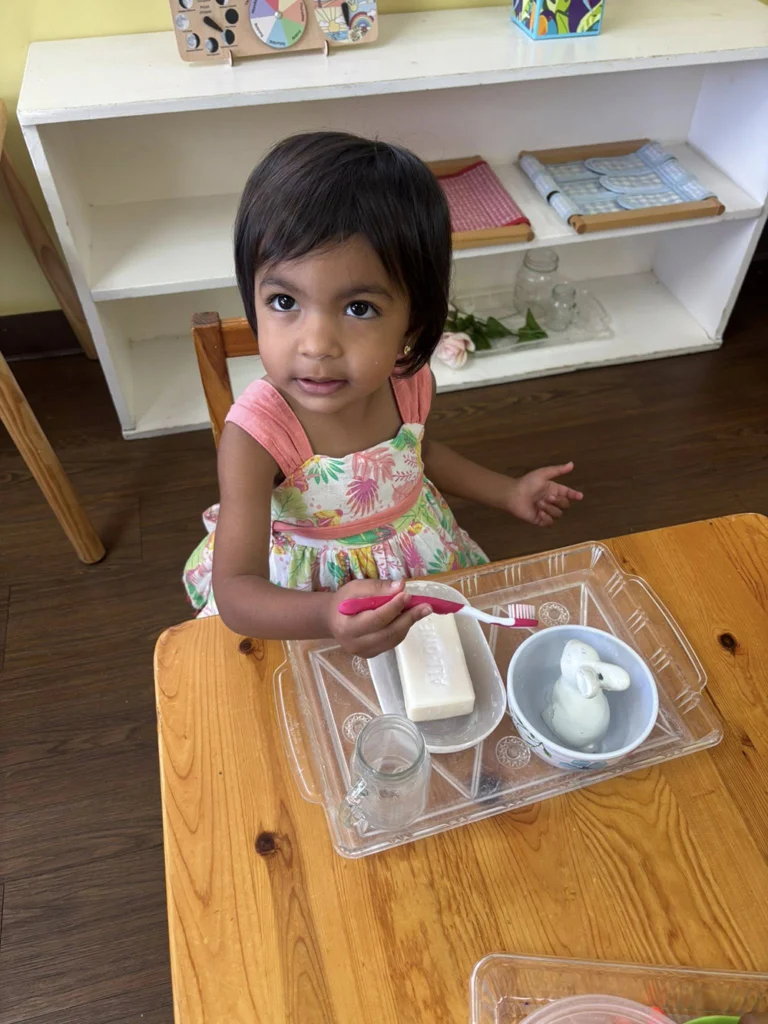 Child using a toothbrush during a Montessori practical life washing activity
