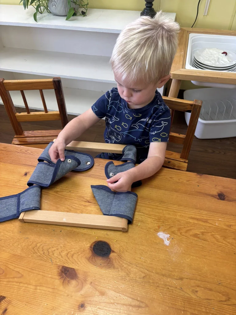 Child practicing fastening skills with a Montessori dressing frame
