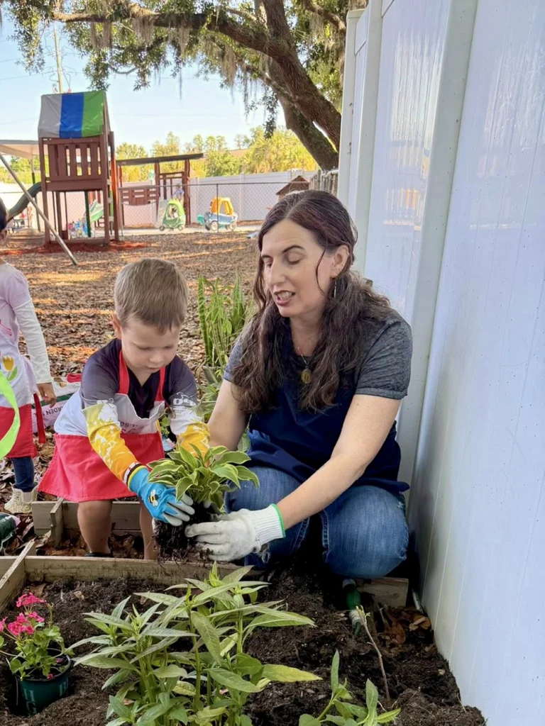 Montessori teacher in the garden guiding a student through transplanting a plant into the garden.
