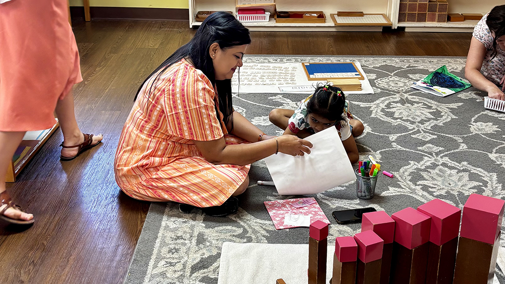 Mother and her daughter looking at classroom supplies on a floor mat for a Montessori activity