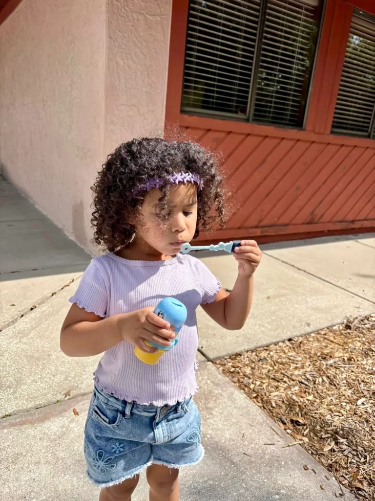 Child on an outdoor playground blowing bubbles.