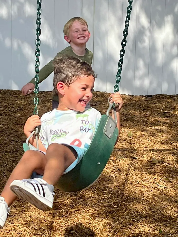 A child at a Montessori school playing on a swing and smiling.