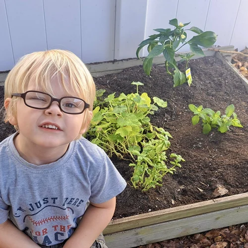 Young Montessori student sitting beside plants in the school garden